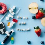A creative diabetes awareness still life with insulin syringe, fruits, donut, and glucose meter on blue background.